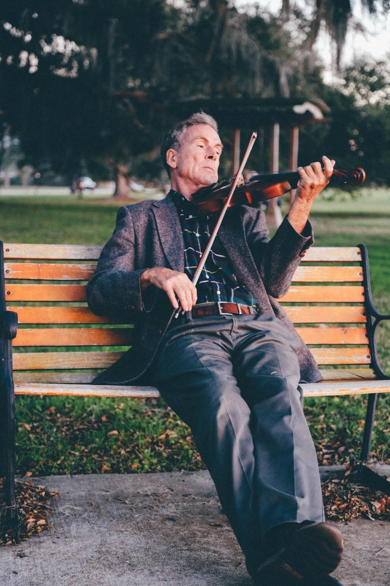 an older man playing a violin on a park bench, _park violin player 4k