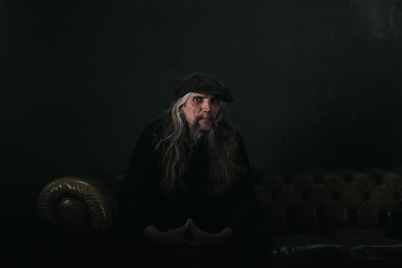 a man with long gray hair sits on a couch against a black background, man with long gray hair 4k