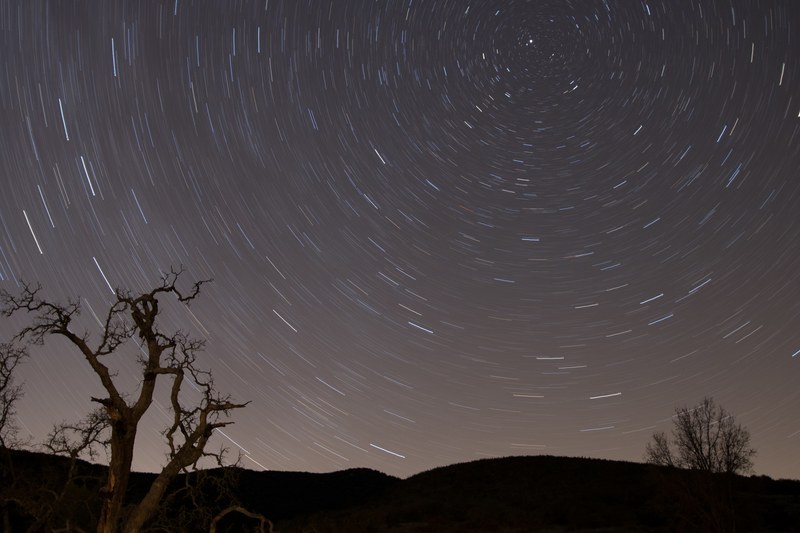a long exposure shot of a star filled night sky featuring silhouette trees and hills, celestial adventure 4k