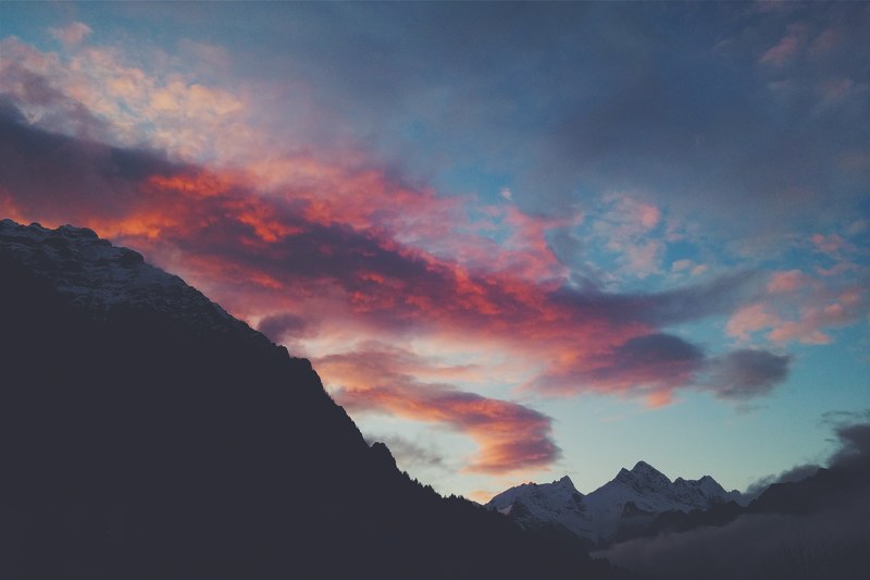 a large red cloud moving through the blue sky over snow capped mountains, red cloud over snowy mountains 4k