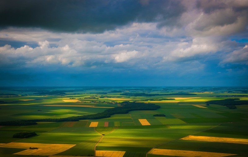 wide shot of green and yellow agricultural fields with clouds overhead, landing in france 4k