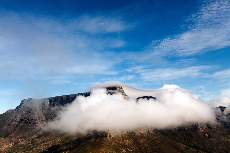 a fluffy cloud enveloping a rocky mountaintop on a bright day, cloud enveloping a mountain 4k