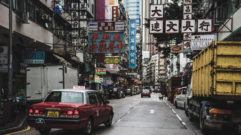 shiny red toyota taxi driving on road in urban street with advertising signs in hong kong, red taxi hong kong street 4k
