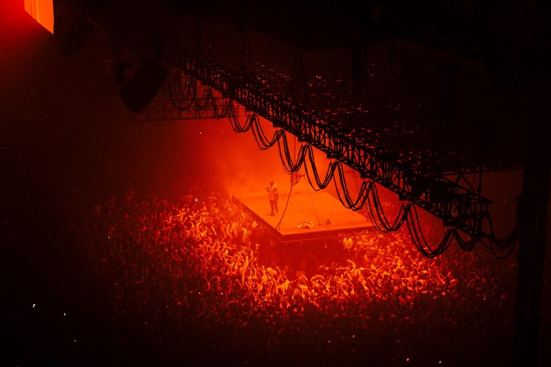 a high shot of a crowd surrounding a suspended stage with a vocalist bathed in red light, suspended stage in red light 4k