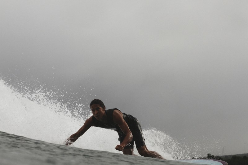a closeup photo of a surfer riding a wave in a wetsuit under a grey sky, preparing to surf the wave 4k