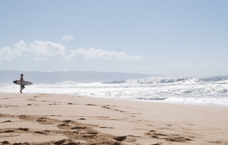 surfer on the sand beach in oahu walking towards rough ocean, north shore 4k