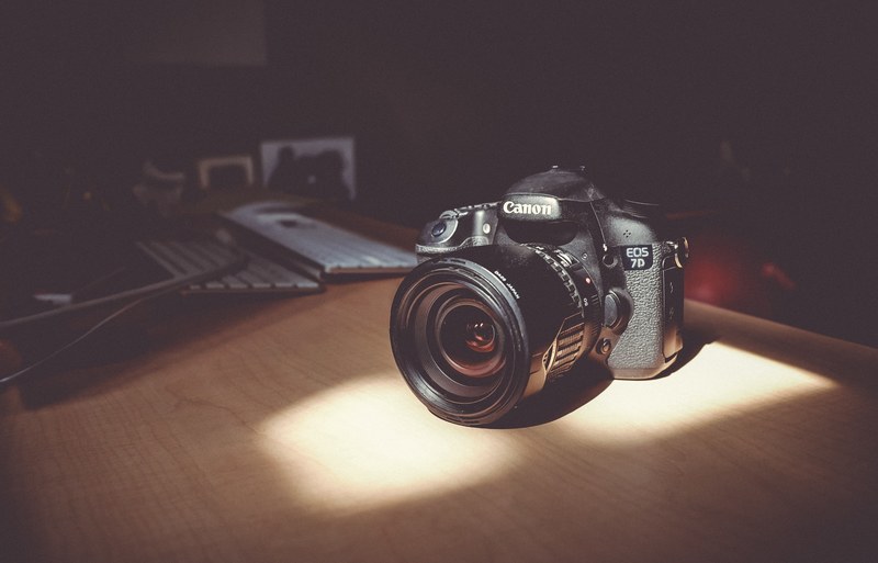canon eos 7d illuminated by daylight coming through a window beside two keyboards on a wooden desk in a dark room, canon eos 7d 4k