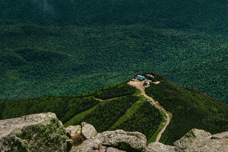a mountainside view of several buildings on a hill overlooking a vast forest, hill seen from a mountain 4k