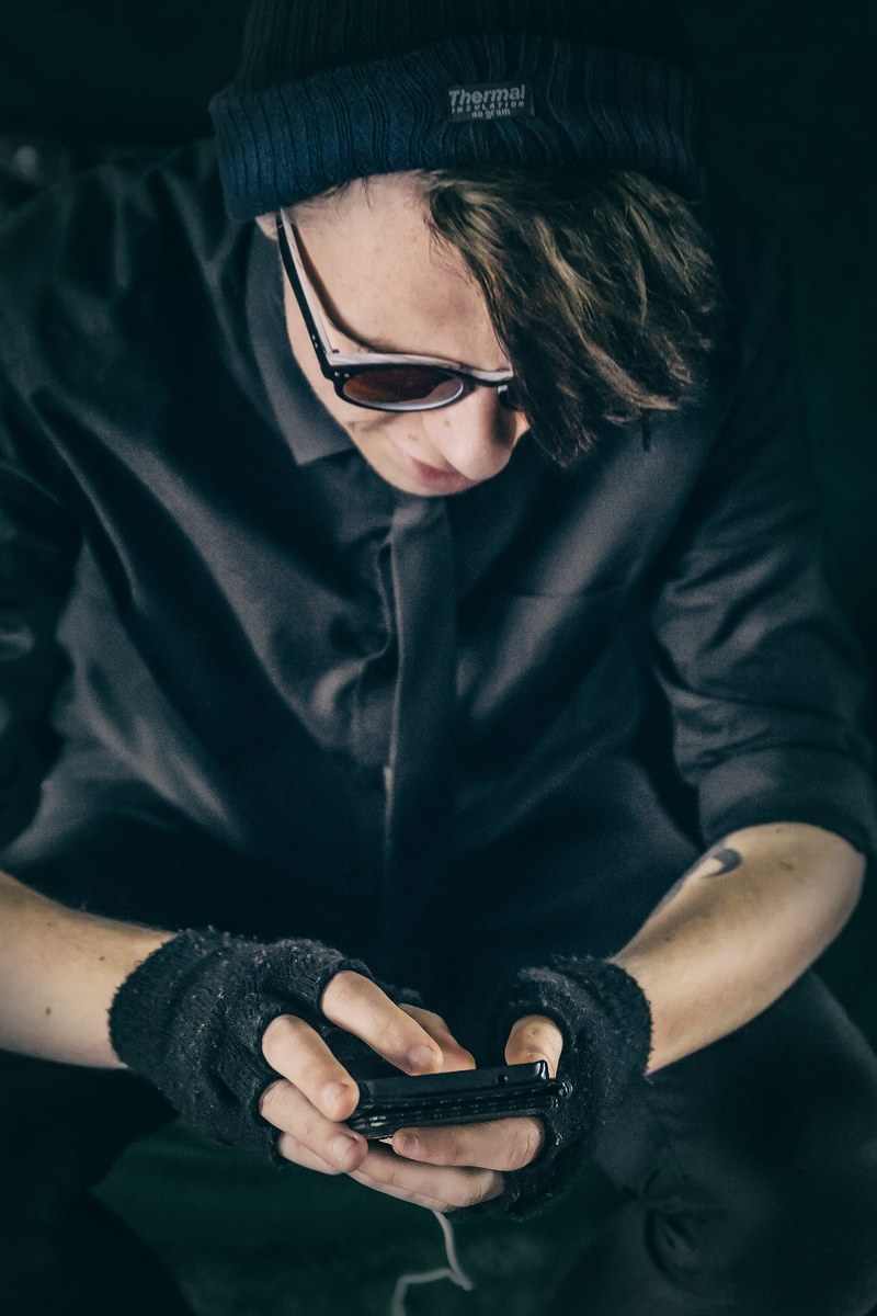 a person in black clothing and fingerless gloves looks down using an iphone, person in fingerless gloves 4k