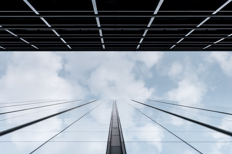 a low angle shot of a glass facade reflecting the clouds in the sky above, clouds in a tall glass facade 4k