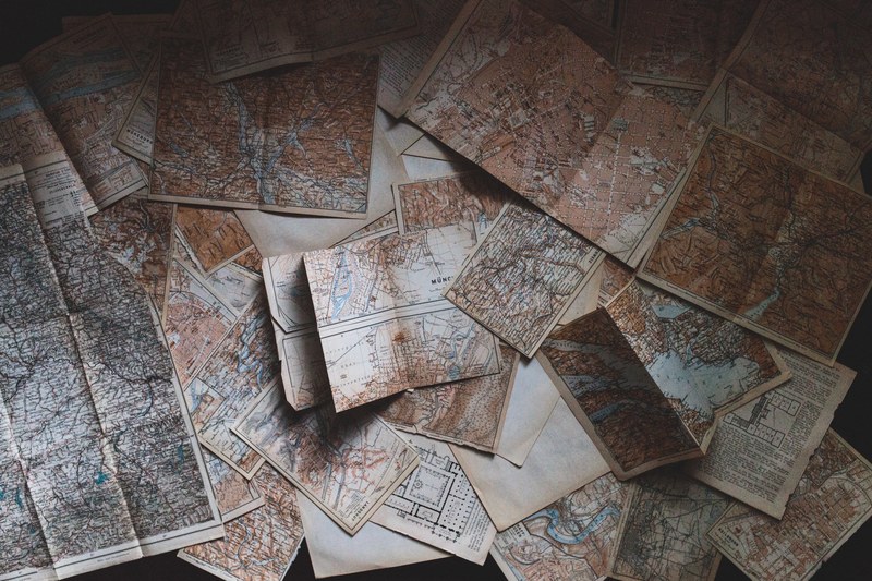 an overhead shot of a large collection of maps scattered on the floor, where to next 4k