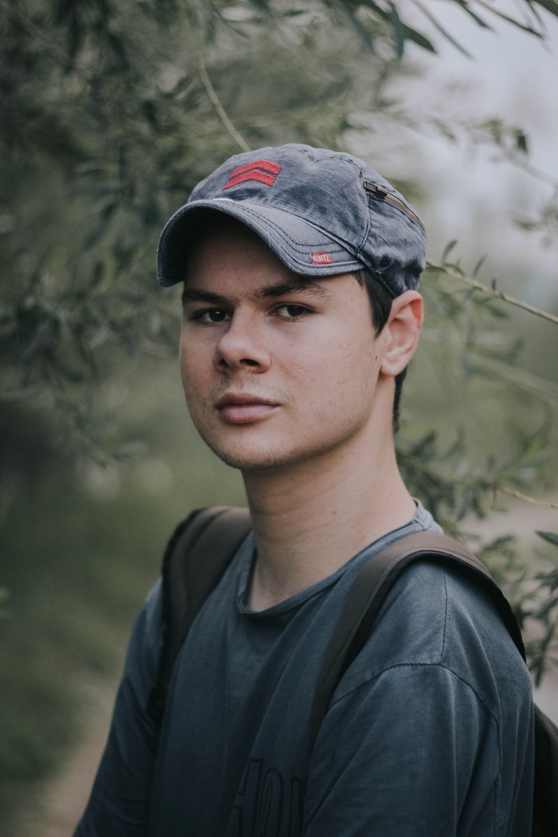 man in a baseball hat and backpack making eye contact outsite, me 4k
