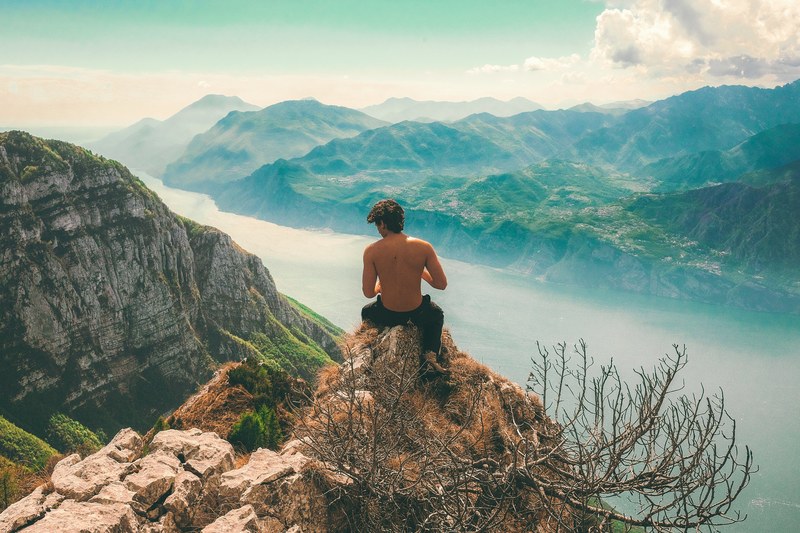 man sits on the edge of a rocky mountain bluff, adventurous views 4k