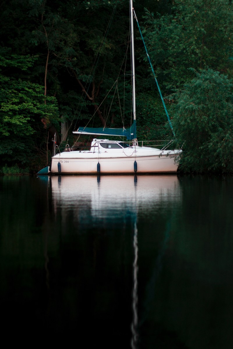 a small yacht moored at the shore of a lake, small yacht on a lake 4k