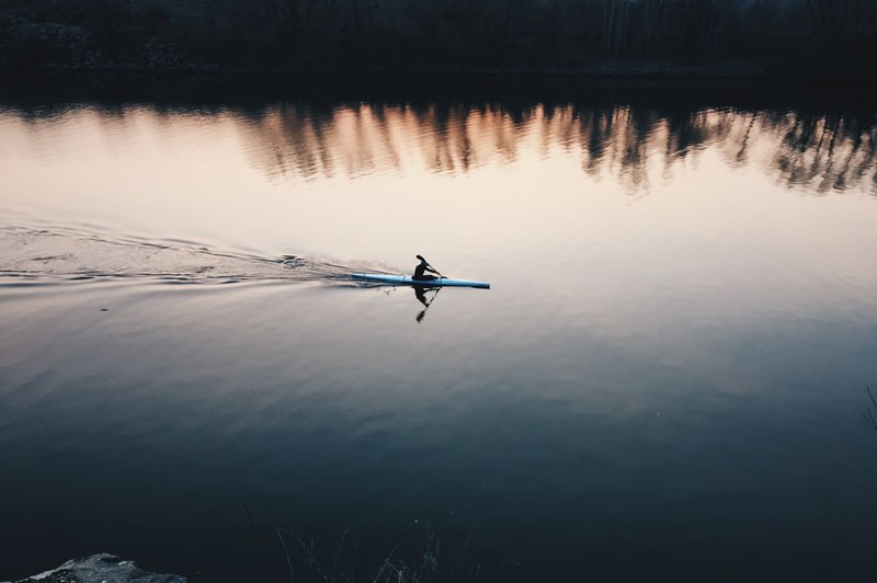 a person in a white kayak on a smooth lake at sunset, evening kayaking 4k
