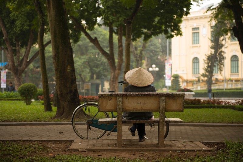 a person wearing a traditional vietnamese hat sitting on a park bench with their bicycle nearby in hanoi, hanoi bench 4k