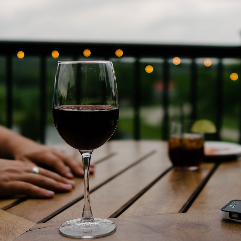 the macro view of red wine in a wine glass in a dinner and hands on table behind it, outdoor wine dinner 4k