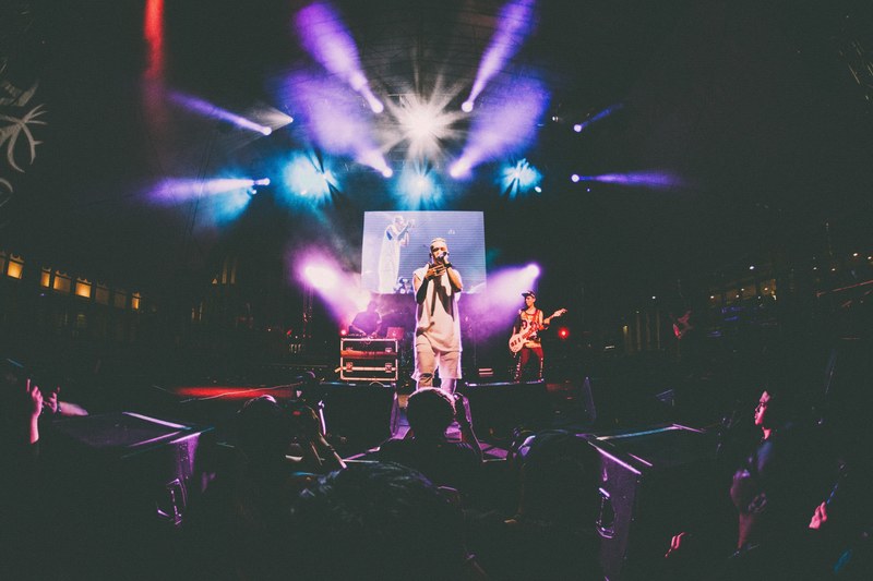 a vocalist sings close to the edge of the stage while band members play instruments at the back, frontman under colorful floodlights 4k