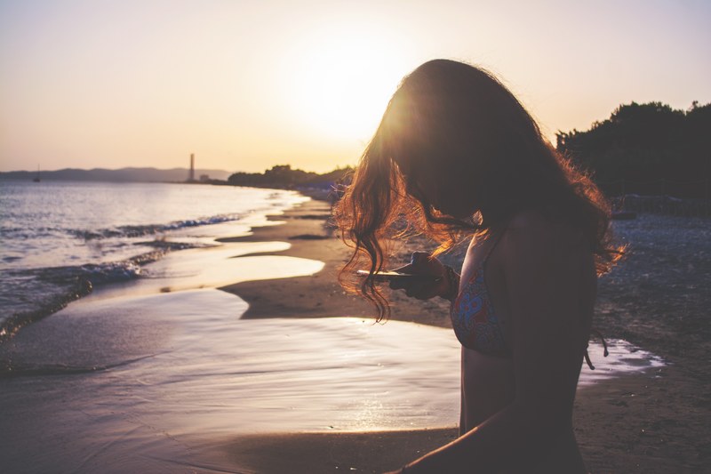 woman in swimsuit typing on the smartphone on the sand beach at sunset in oasi sosta camper, woman with smartphone on beach 4k