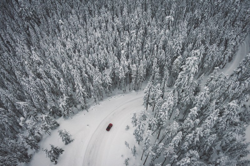 aerial drone view of a car on a winding snow covered road through pine forest in mount hood national forest, above the frozen forest 4k