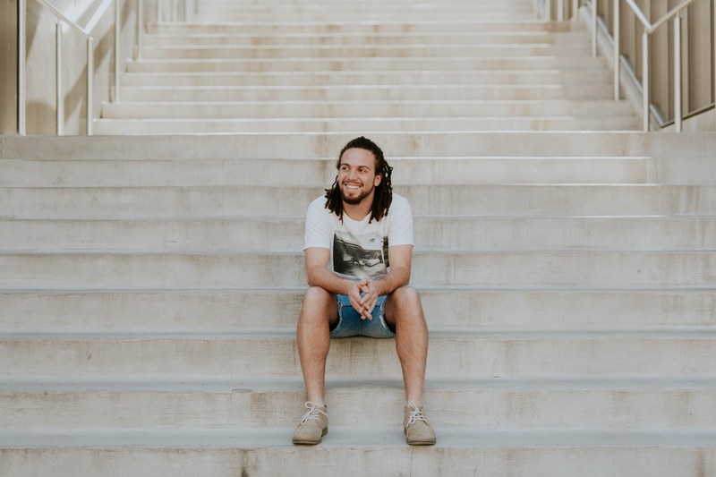a man with dreadlocks smiles while sitting on steps at the university of arkansas, man smiling on steps 4k