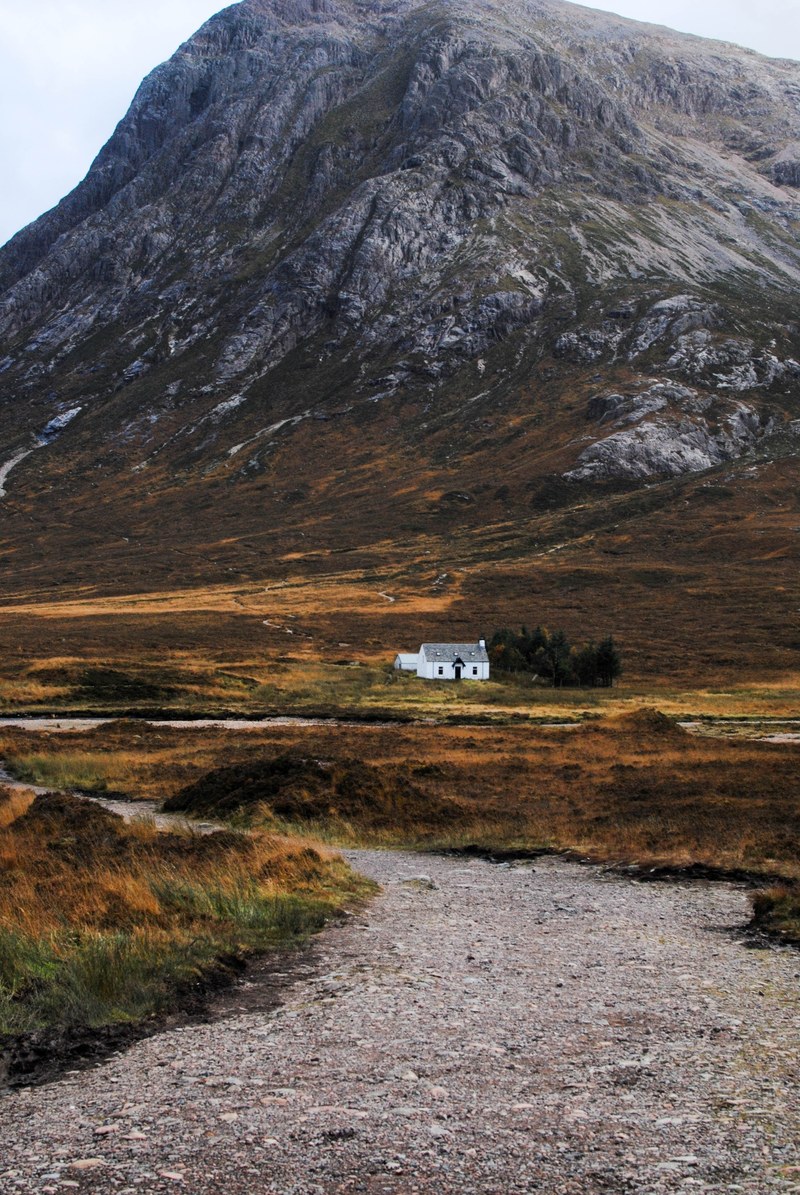 a small white building on a grassy plain at a rugged mountains foot, white house in the highlands 4k