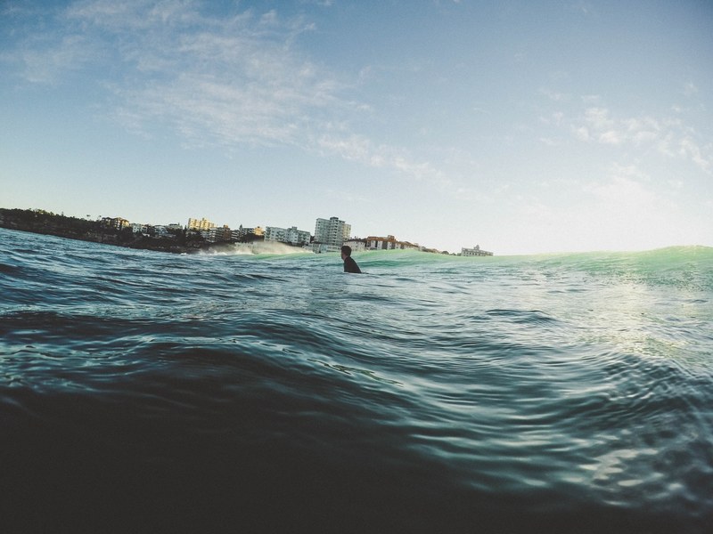 person floating in the ocean by the coast at bondi beach, bondi beach surfer 4k