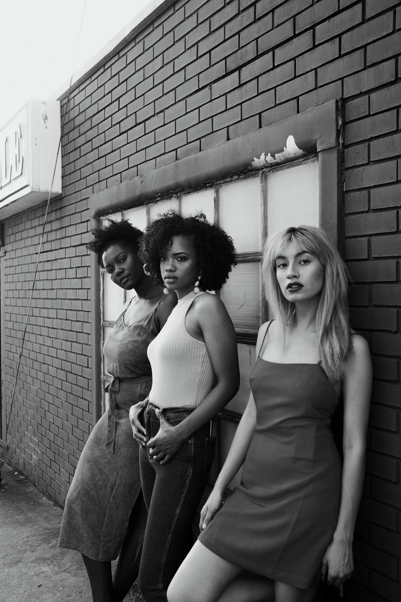 one woman and two of her friends standing in front of a brick wall, women in front of a brick wall 4k