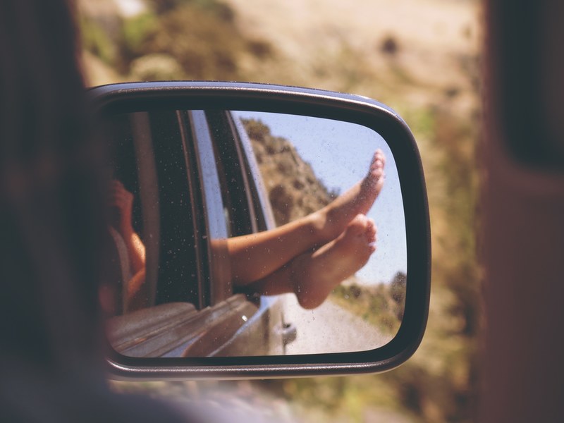a person sticking their feet out of a car window from the perspective of the rear view mirror, sticking feet out car window 4k