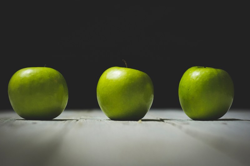 three green apples in a row on a table, row of apples 4k