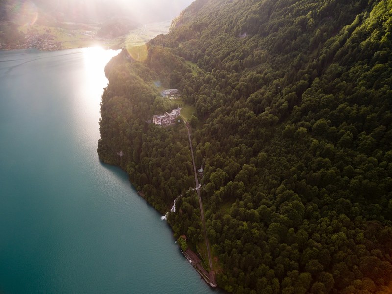 a drone shot of a hotel on a wooded shore of a lake, grandhotel giessbach am brienzersee 4k