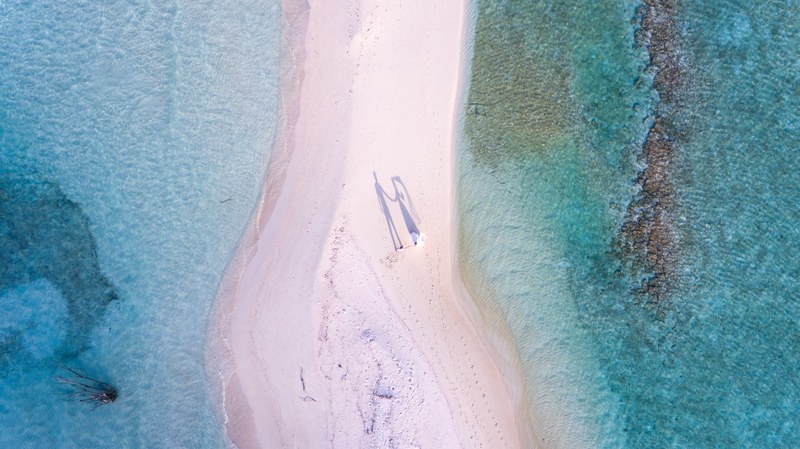 drone aerial view of newly wed couple on the sand beach stretch by the ocean at the north central province maldives, wedding photography in maldives by ishan 4k