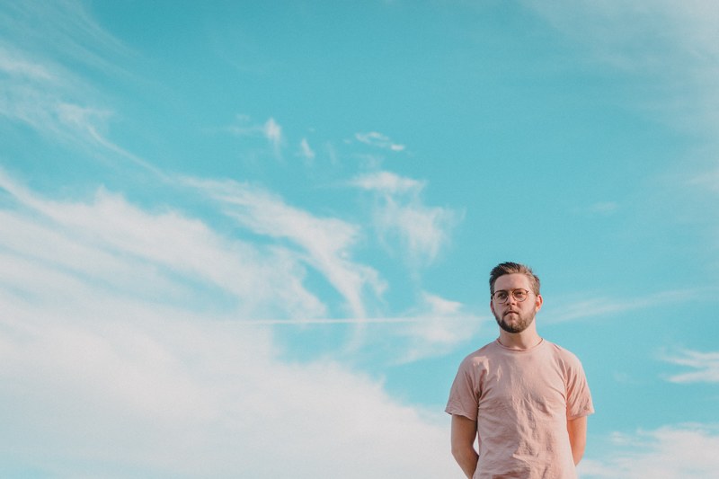 man in hipster glasses standing against a blue sky with clouds, spectacles and sky 4k