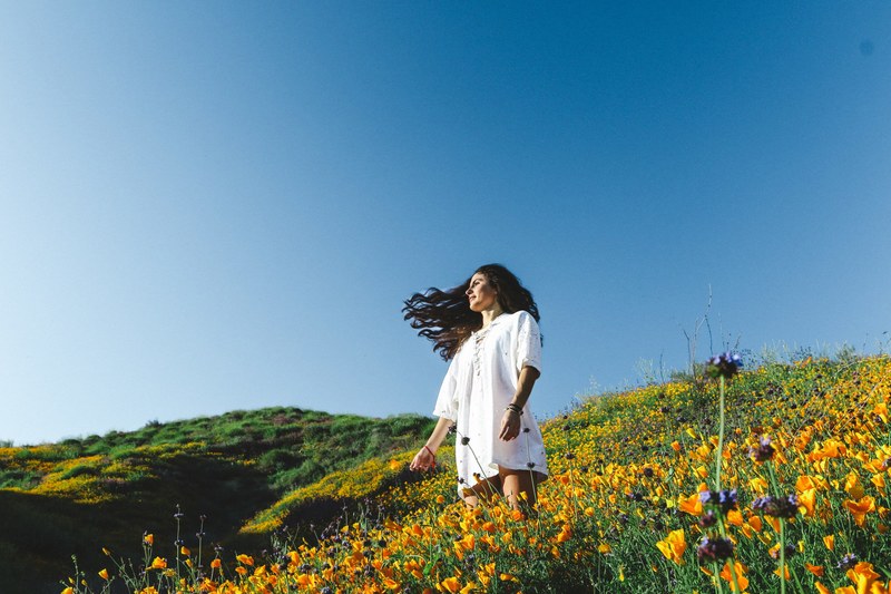 a dark haired woman in a white dress in a sunny meadow full of orange flowers, woman in a sunlit meadow 4k