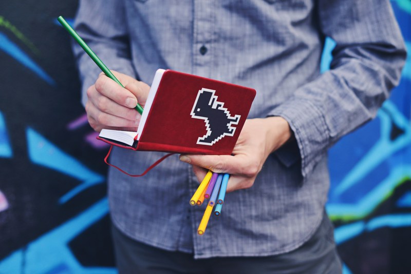 a person taking notes in a red notebook with a dinosaur on its cover while standing, when your internet is down 4k