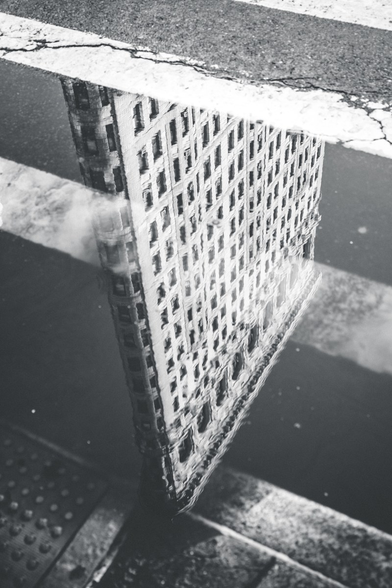 black and white shot of flatiron building reflection in puddle on road, flat lines 4k