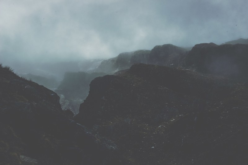 fog rolls in over dark stone mountains in mount aspiring national park, overcast mountains 4k