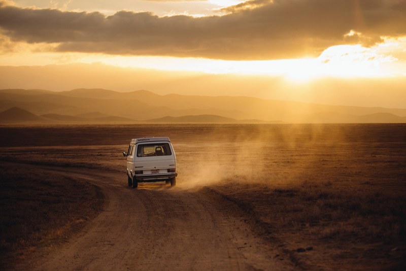 a white car driving along a curve in a dusty road in the outback, road dust under setting sun 4k