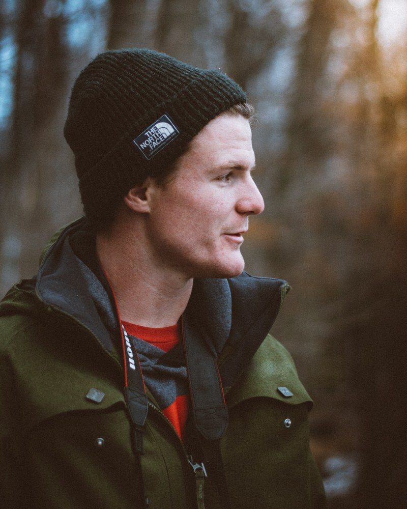 a man in a north face cap wears a nikon camera strap around his neck outdoors, man wearing camera strap 4k