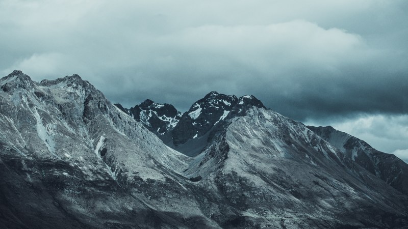 a bleak shot of snow capped mountains under thick gray clouds, queenstown peak 4k