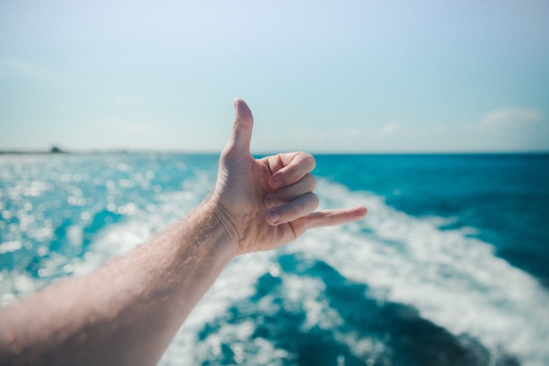 an outstretched hand making a telephone gesture over the white wake left in the sea by the boat, hang loose 4k
