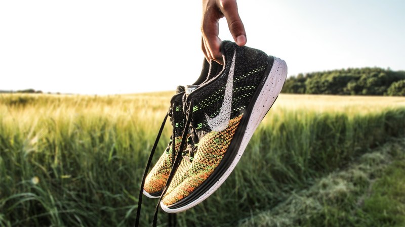 a person holding a pair of nike trainer shoes in a field, holding a pair of nike shoes 4k