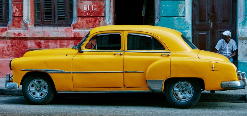 parked vintage yellow car on street in havana with an onlooking man in the background, yellow vintage car havana 4k