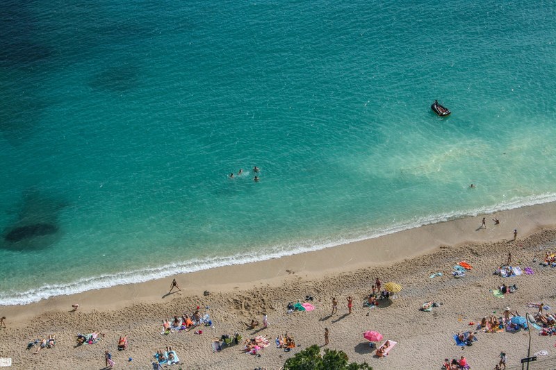 an aerial shot of people sunbathing on a wet beach with a group of friends swimming in the sea, holiday on a wet beach 4k