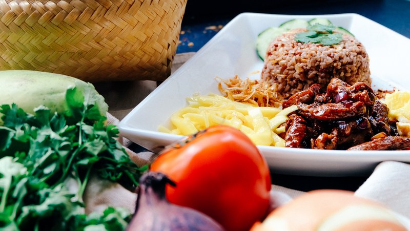 rice noodles and beef on a white plate with a tomato onion and herbs next to a whicker basket, rice and meat for dinner 4k