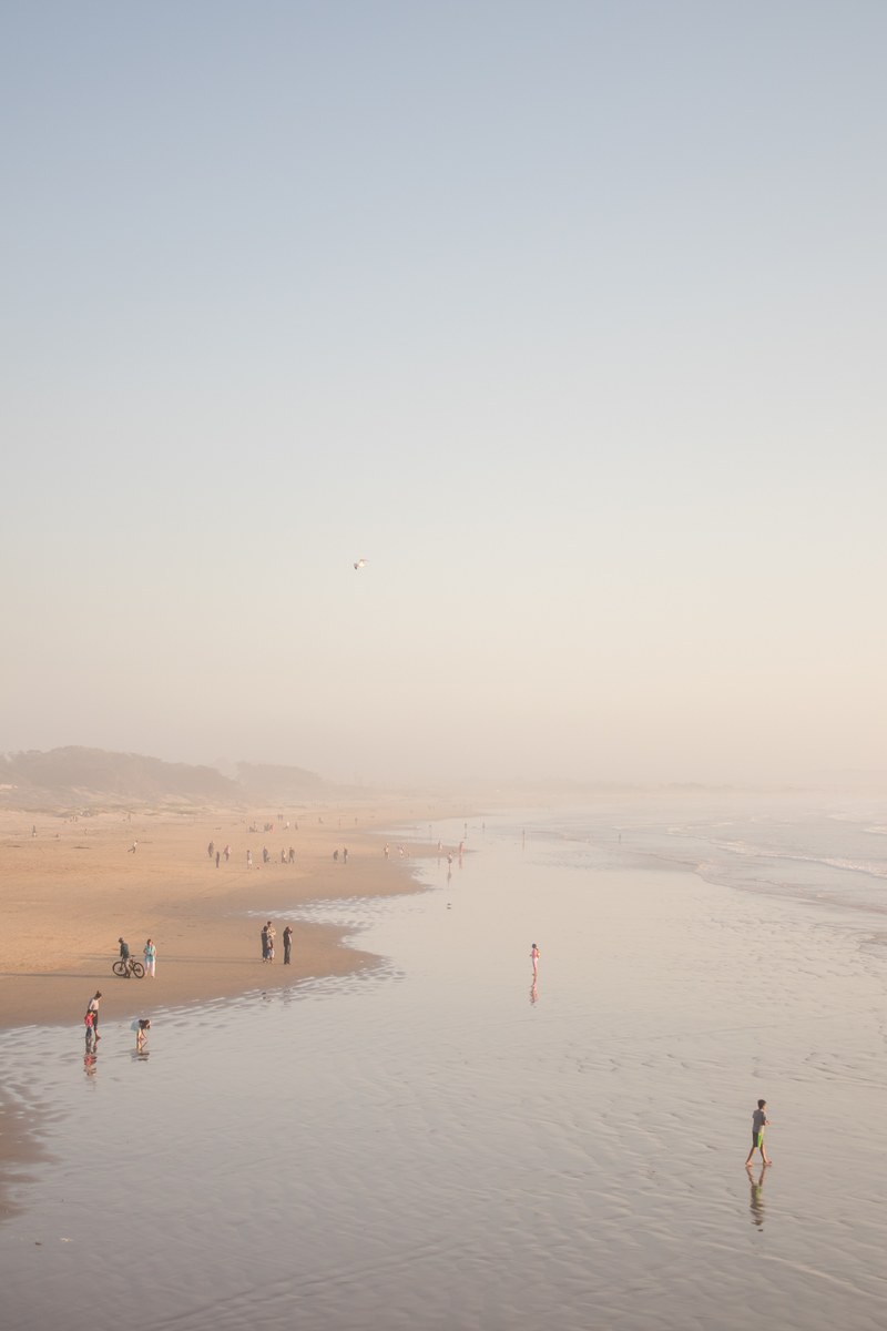people on the vast sand coastline with ocean washing ashore, endless 4k