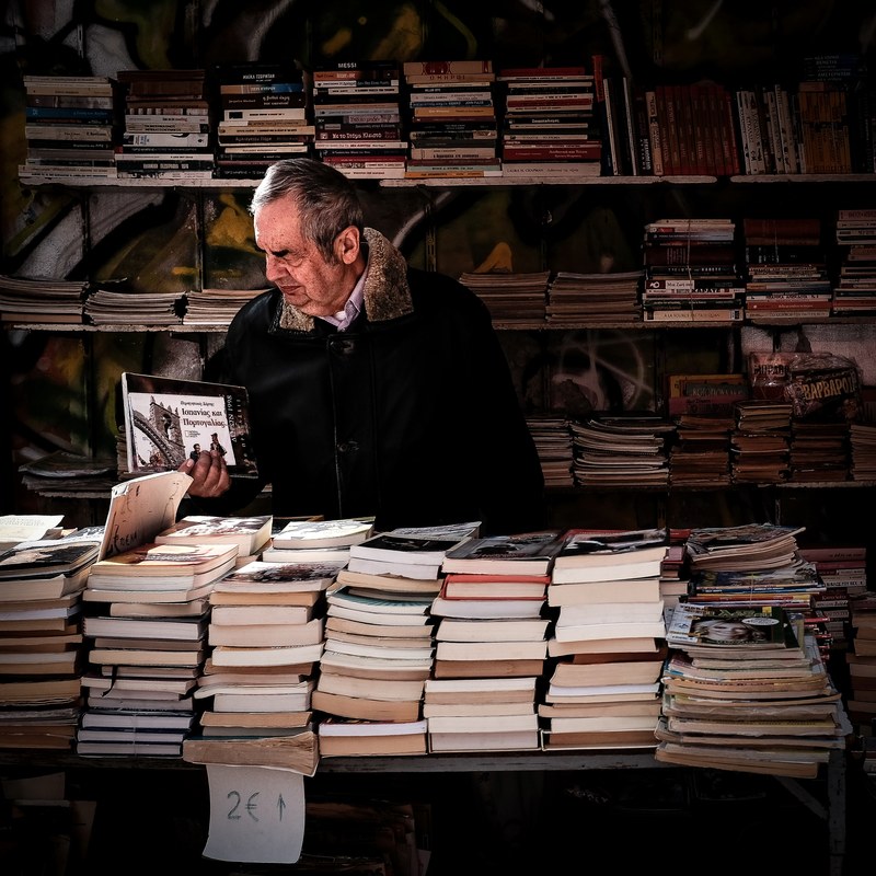an elderly man browsing books in a bookstore in athens, elderly man in a bookstore 4k