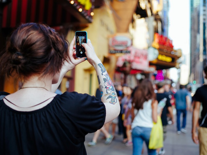 a woman with a tattoo on her arm taking a photo of the times square, photographing times square 4k