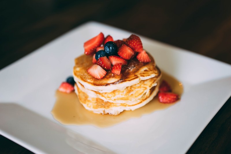 a stack of golden brown pancakes covered in syrup and fresh strawberries and blueberries on a white plate, pancakes with berries 4k