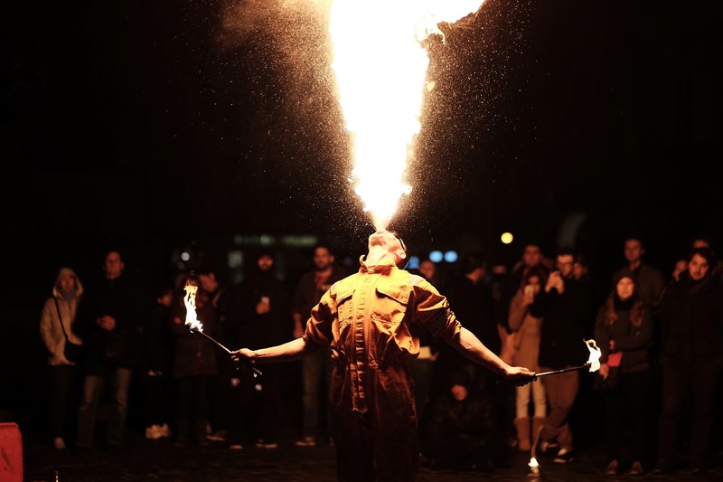man holding torch and blowing fire out of mouth with people standing behind him, fire breathing 4k